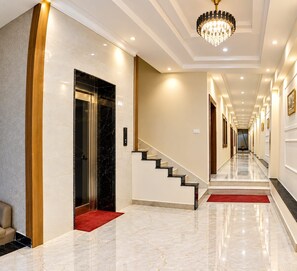Un pasillo de hotel con piso de mármol, alfombra roja, una escalera y un candelabro.
