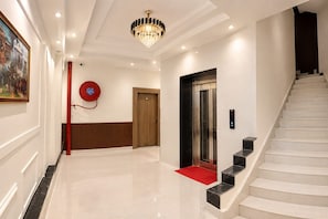 A modern hotel lobby with a marble floor, a chandelier, a red fire extinguisher, a wooden door, an elevator, and a staircase. - Hotel Dream Kashi (Faizabad)