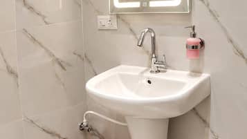 Un baño con lavamanos pedestal blanco, un espejo con iluminación integrada, un cubo de basura rojo y un recipiente de plástico transparente.
