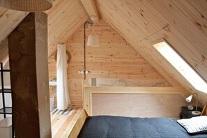 A wooden room with a sloped ceiling, a bed with a headboard, a small bedside table, a lamp, and a window. - Holiday home in Tangermünde with Wi-Fi (Tangermünde)