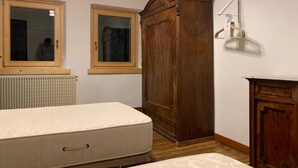 A bedroom with a bed, a wooden wardrobe, a radiator, and two windows. - Casa Le Triestine: cozy, traditional Dolomite accommodation for groups (Venas di Cadore)