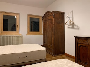 Ein Schlafzimmer mit einem Bett, einem Holzschrank, einem Heizkörper und zwei Fenstern.