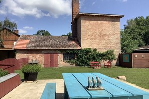 Een bakstenen gebouw met een pannendak, een houten hek en een picknicktafel met een sculptuur.