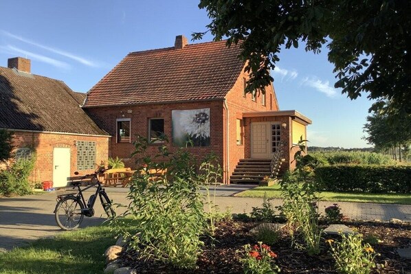 Een bakstenen huis met pannendak, een fiets en een tuin vol bloemen en planten.