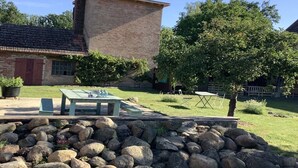 A brick building with a chimney, a stone wall, and a grassy area with a table and chairs. - Holiday home with 5 bedrooms (Trebel, Niedersachsen)