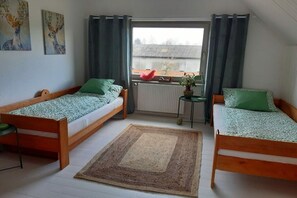 Een kamer met twee houten bedden, een tafeltje, een radiator en een raam met gordijnen.