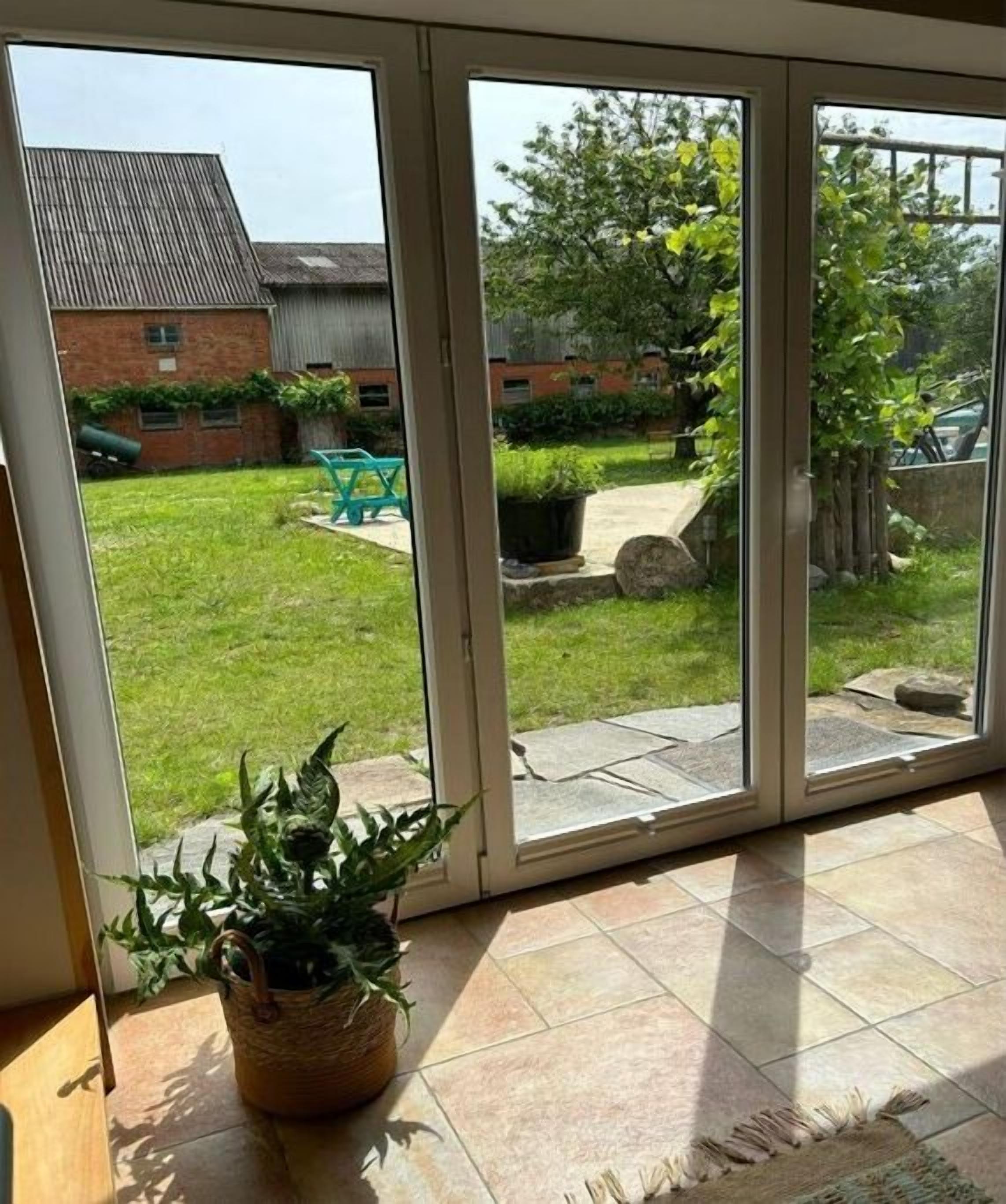 A view through a glass door into a backyard with a grassy lawn, a brick building, and a blue chair.