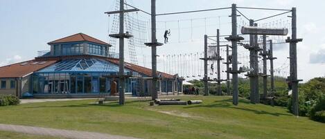 A building with a glass facade and a red roof, surrounded by a grassy area and a rope course.