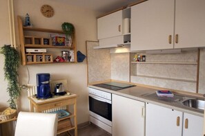 Een kleine keuken met witte kastjes, een inbouwoven, een koffiezetapparaat en een klok aan de muur.