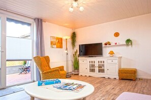 Ein Wohnzimmer mit Fernseher, einer Couch, einem Couchtisch und einem Fenster mit Jalousien.