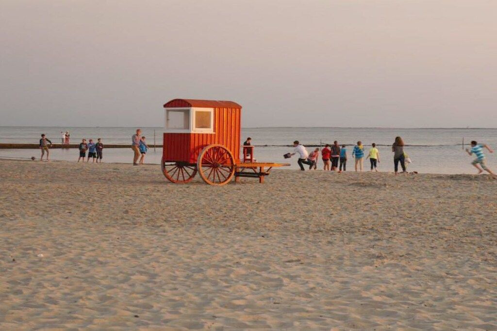 A beach with a red and white structure, possibly a lifeguard station, and people walking along the shore.