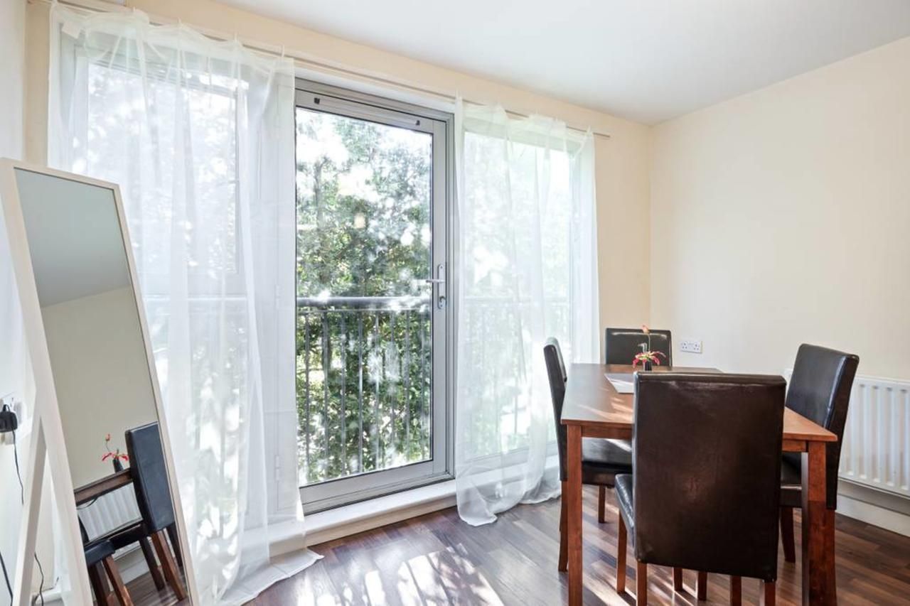 A room with a dining table, chairs, a window with sheer curtains, and a radiator.