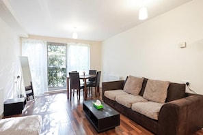 Een woonkamer met een bruine bank, een bijzettafeltje, en een eethoek met stoelen en een tafel.