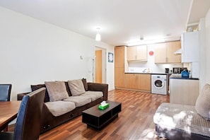 Een gezellig compact leefruimte met een bank, een salontafel, een eettafel en een keukenhoek, inclusief een wasmachine.