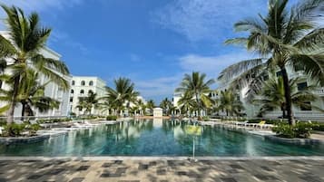 Zona de piscina en un resort, con palmeras y cielo despejado.