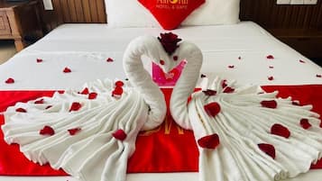 Ein Hotelzimmer mit einem Bett, einem roten Kopfkissen mit der Aufschrift 'AMORII HOTEL & CAFE' und einer Handtuchgestaltung in Form von Schwänen mit Rosenblättern.