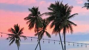 A beach scene with palm trees, a string of lights, and a boat on the sand. - Amorii Hotel Phu Quoc (Phu Quoc)