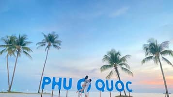 Eine Strandansicht mit Palmen und dem Schriftzug 'PHU QUOC' im Sand.