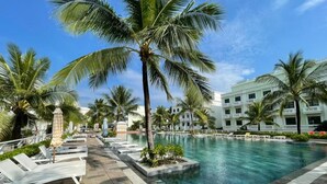 A pool area with lounge chairs and palm trees, surrounded by a building with multiple windows. - Amorii Hotel Phu Quoc (Phu Quoc)