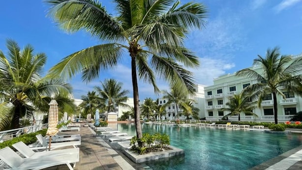 A pool area with lounge chairs and palm trees, surrounded by a building with a white facade. - Amorii Hotel Phu Quoc (Phu Quoc)