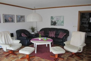 A living room with a black leather sofa, two white armchairs, a white coffee table, and a floor lamp. - Holiday home in Aurich with swimming pool (Aurich)