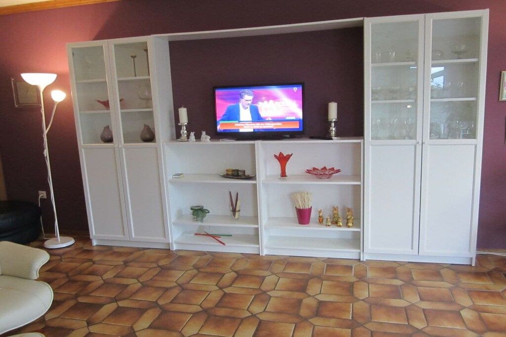 Un salon avec un téléviseur posé sur un meuble, des étagères blanches et un sol à motifs.