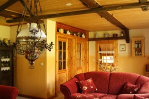 A cozy room with a wooden ceiling, a hanging chandelier, a red sofa, and wooden cabinets with kitchenware. - Holiday home with 1 bedroom (Neuenkirchen)