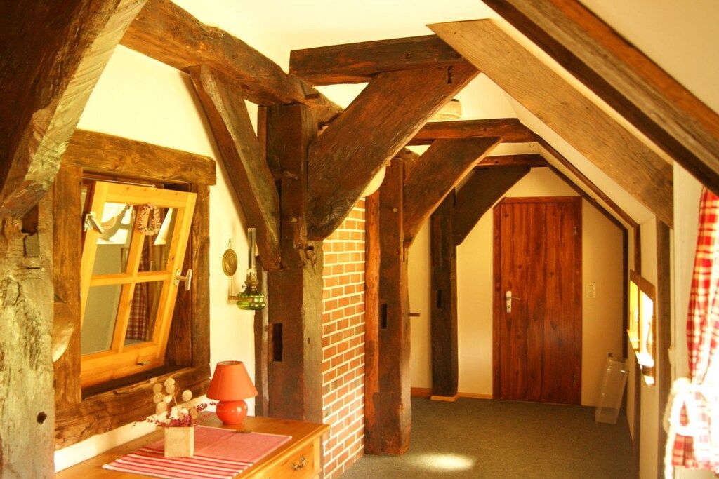 A room with exposed wooden beams, a brick wall, a wooden door, and a window with curtains.
