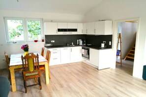 Eine moderne Küche mit weißen Schränken, einer schwarzen Arbeitsplatte und einem Essbereich mit Holztischen und einem Tisch.