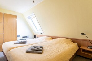 A hotel room with two beds, a desk, a chair, a window, and a lamp. - Apartment with 1 bedroom (Hollum Ameland)