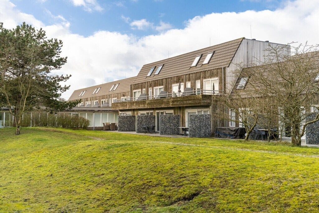 A modern building with multiple levels, a flat roof, and a large grassy area in front.