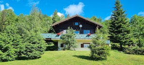 Eine Holzchalet mit Balkon, umgeben von üppiger Vegetation.