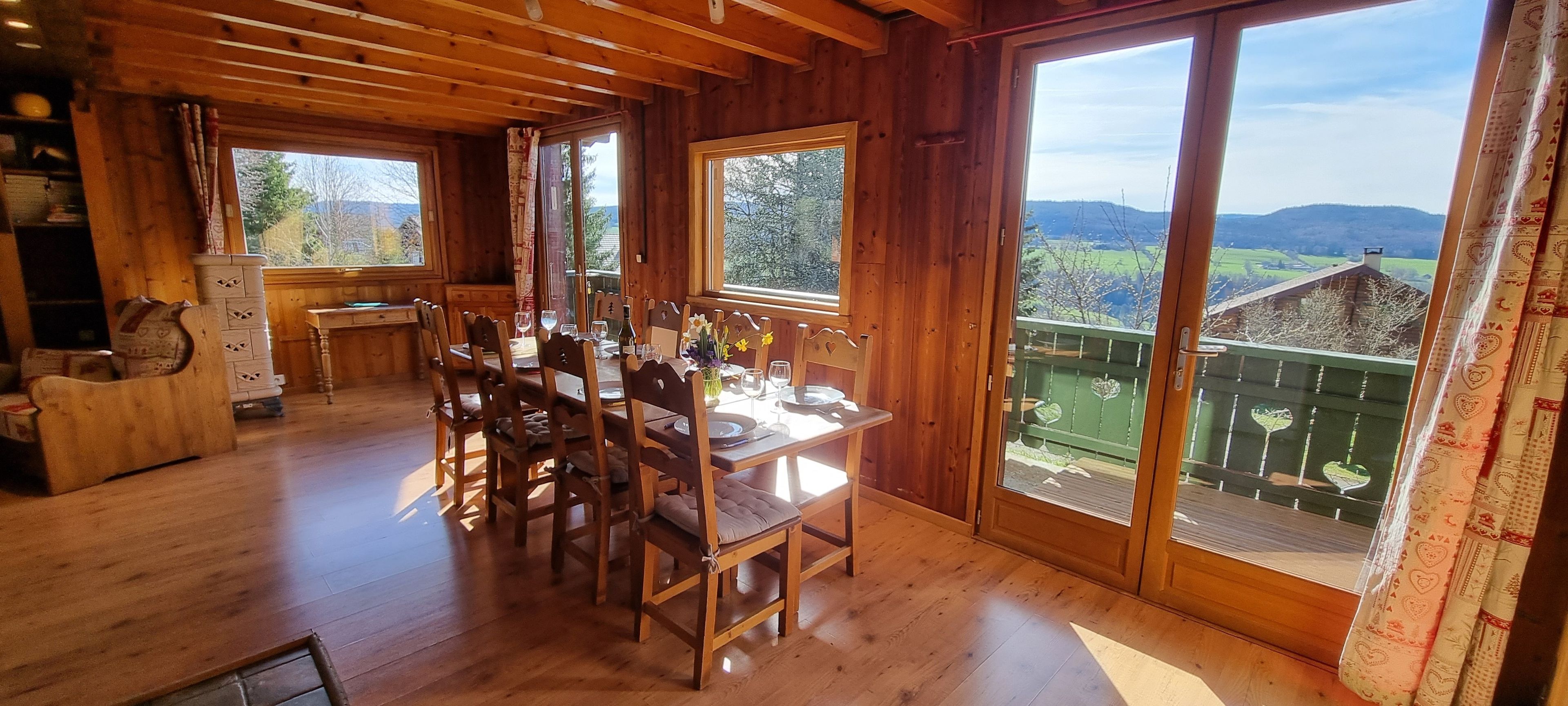 A wooden dining area with a table set for four, large windows, and a view of the countryside.