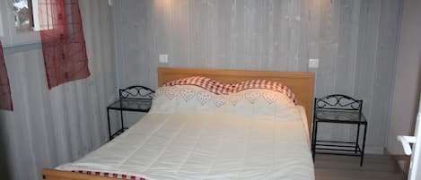 A bedroom with a wooden bed, two bedside tables, a wall-mounted painting, and a window with a curtain.