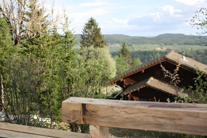 A wooden cabin with a sloped roof, surrounded by dense forest and a view of rolling hills. - Chalet 'Le De Marie': Mountain View, Shared Terrace, and Wi-Fi (Foncine-le-Haut)