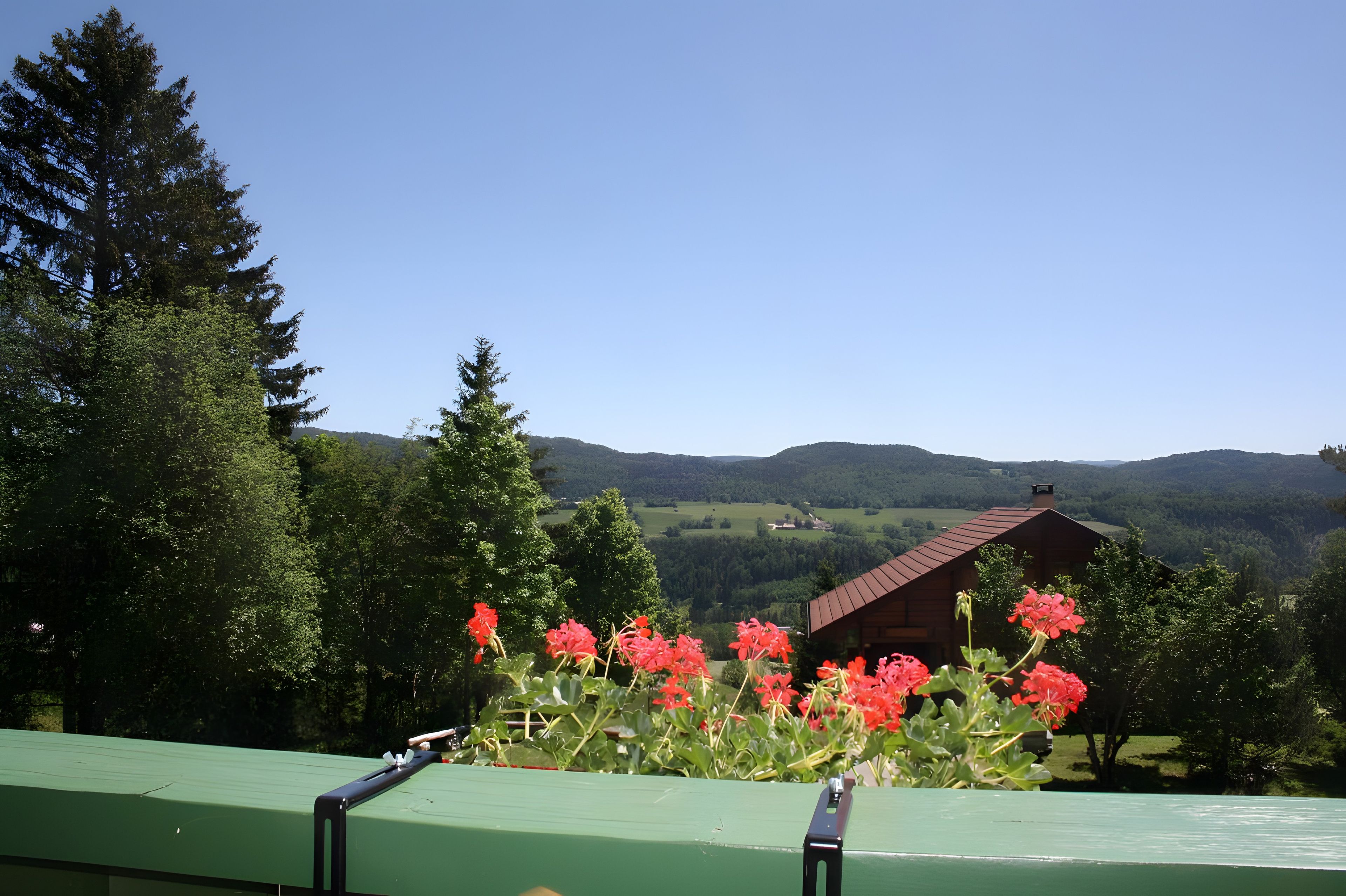 A wooden cabin with a sloped roof, surrounded by lush greenery and mountains in the background.