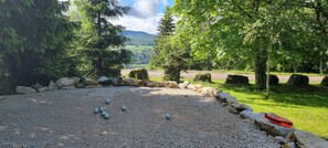 A gravel area with stones and a red object, surrounded by trees and a road. - Chalet 'Le De Marie': Mountain View, Shared Terrace, and Wi-Fi (Foncine-le-Haut)