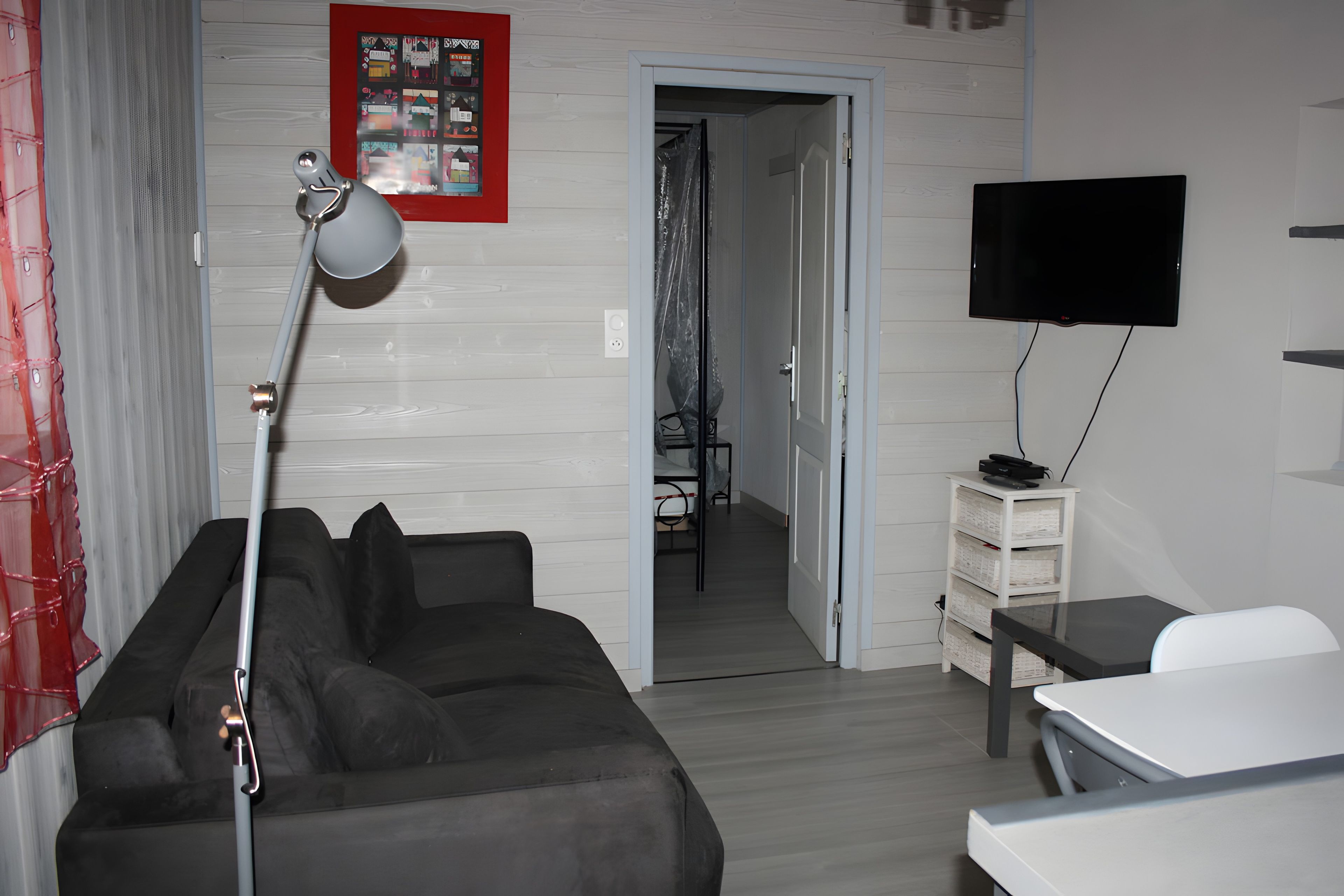 A modern living room with a grey sofa, a desk, a TV, and a door leading to another room.