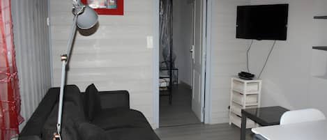 A modern living room with a grey sofa, a desk, a TV, and a door leading to another room.