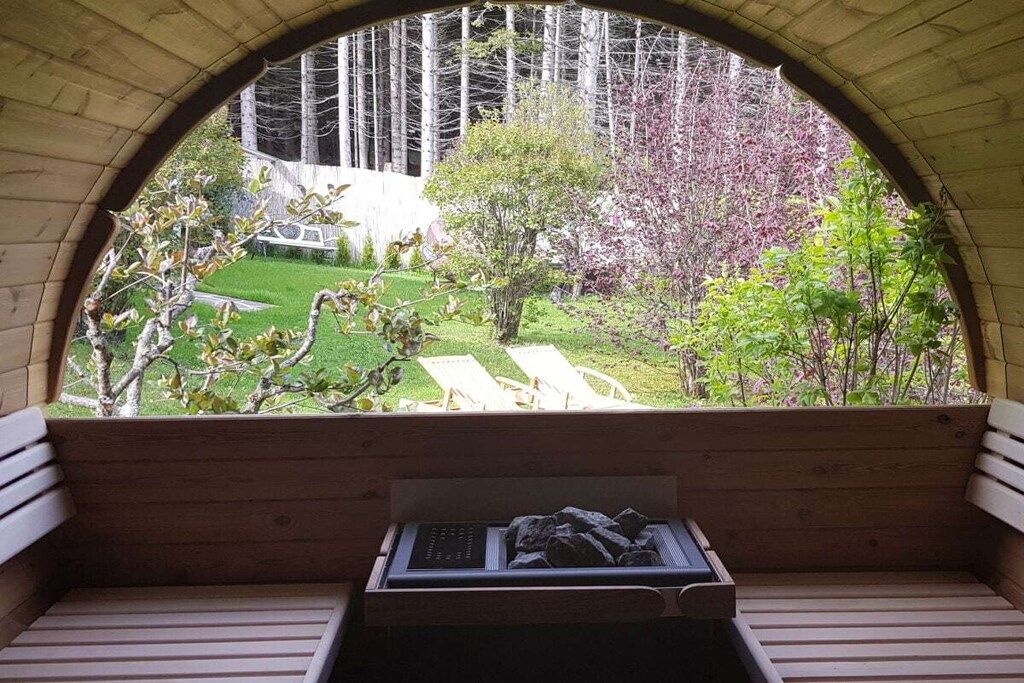 Un banc en bois doté d’un système de chauffage intégré, donnant sur un jardin avec une pelouse, des arbres et une structure blanche.