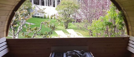 A wooden bench with a built-in heating element, overlooking a garden with a lawn, trees, and a white structure.