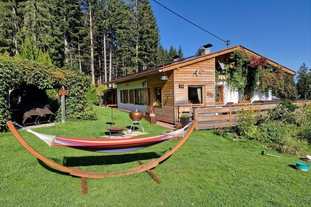 Uma cabana de madeira com uma rede no quintal, rodeada por árvores.