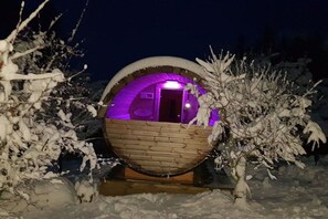 Eine schneebedeckte, kugelförmige Struktur mit Holzaußenverkleidung und violettem Innenlicht.