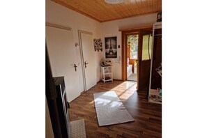 Een kamer met houten vloer, een witte deur, een klein wit plankje en een vloermat.