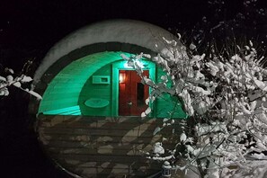 Een koepelvormige constructie met een zichtbare ingang en een deur, omgeven door met sneeuw bedekte takken.