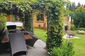Ein Essbereich im Freien mit einer Pergola, die dicht mit Grün bewachsen ist, einem Holztisch und Stühlen.