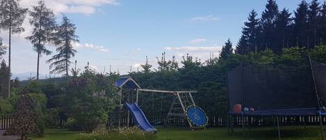 A playground with a slide, swing set, and trampoline in a grassy area with trees.