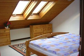 A bedroom with a sloped ceiling, skylights, a wooden bed, a dresser, and a radiator.