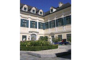 A classical building with symmetrical architecture, multiple windows with shutters, and a well-maintained garden with yellow flowers. - "Vienna Woods" Am Wiesengrund (Wien)