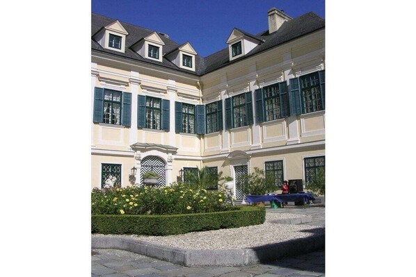 A classical building with symmetrical architecture, multiple windows with shutters, and a well-maintained garden with yellow flowers.